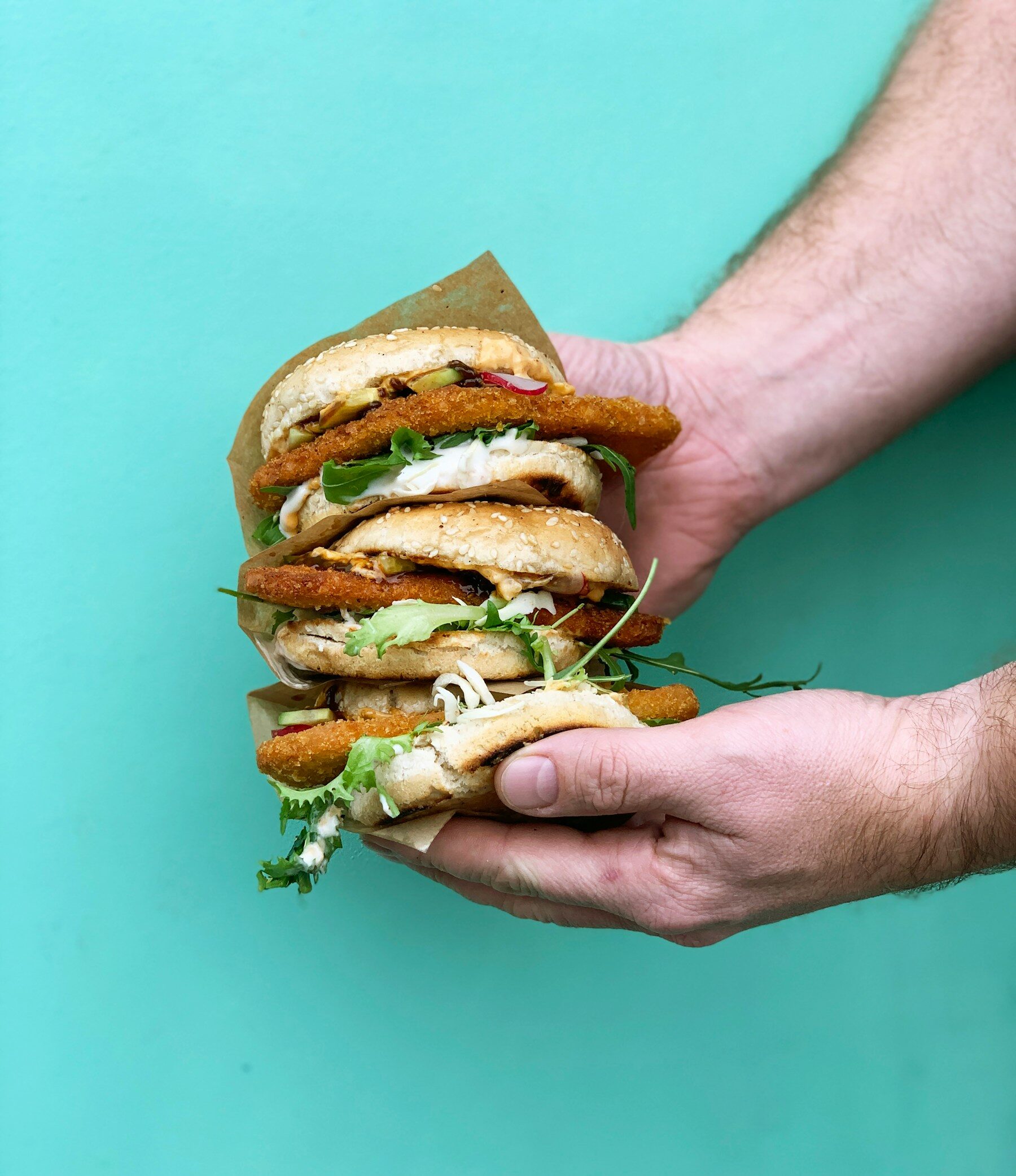 person holding burger with lettuce and tomato