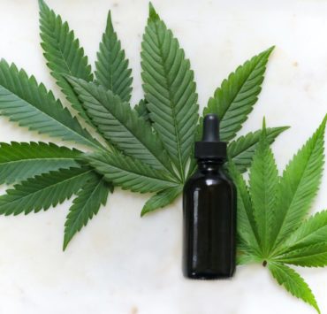 green cannabis leaves and black glass drops bottle