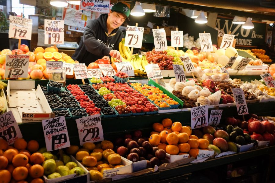 man in black jacket standing in front of fruit stand