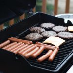 person standing in front grill grilling sausage