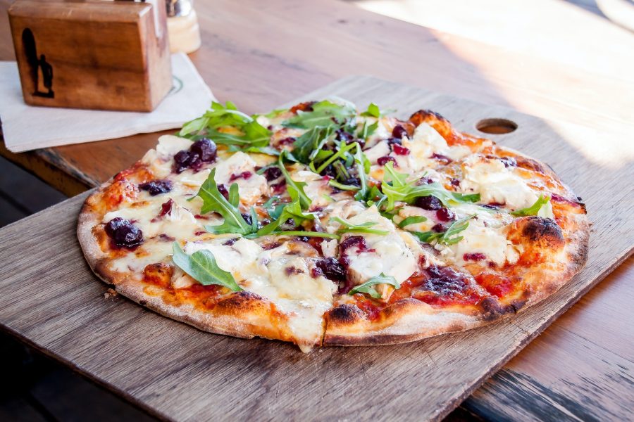 pizza with green and red vegetable on brown wooden table