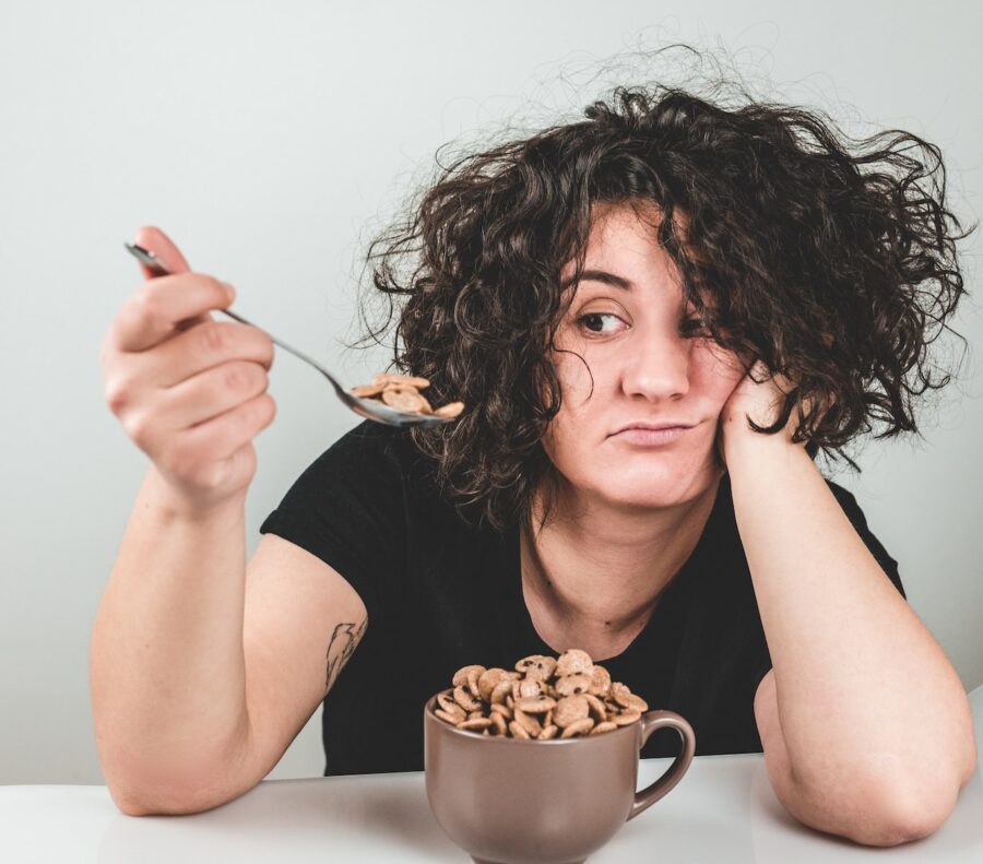 nighttime eating, woman with messy hair wearing black crew-neck t-shirt holding spoon with cereals on top