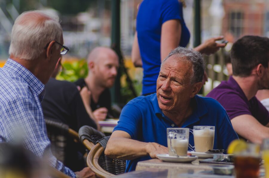 man in blue polo shirt talking to man while drinking coffee, baby boomer consumers