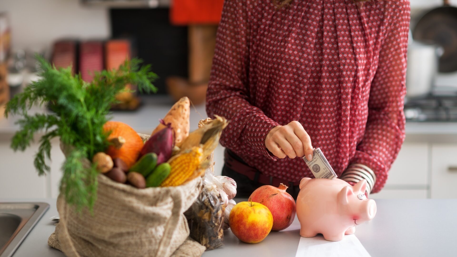 Woman puts money into piggy bank because of inflation. Next to her are groceries.