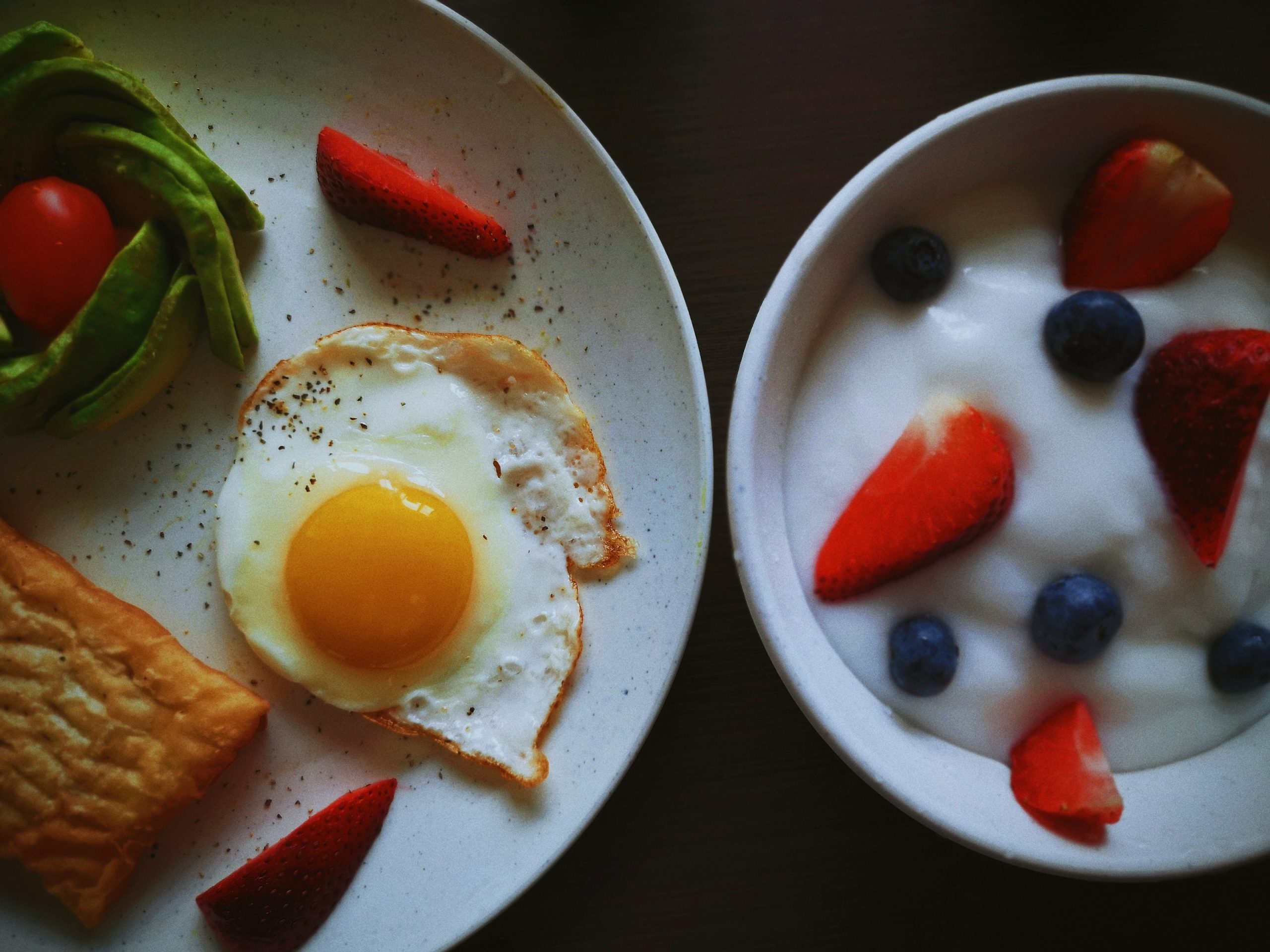 a white plate topped with a fried egg next to a bowl of fruit