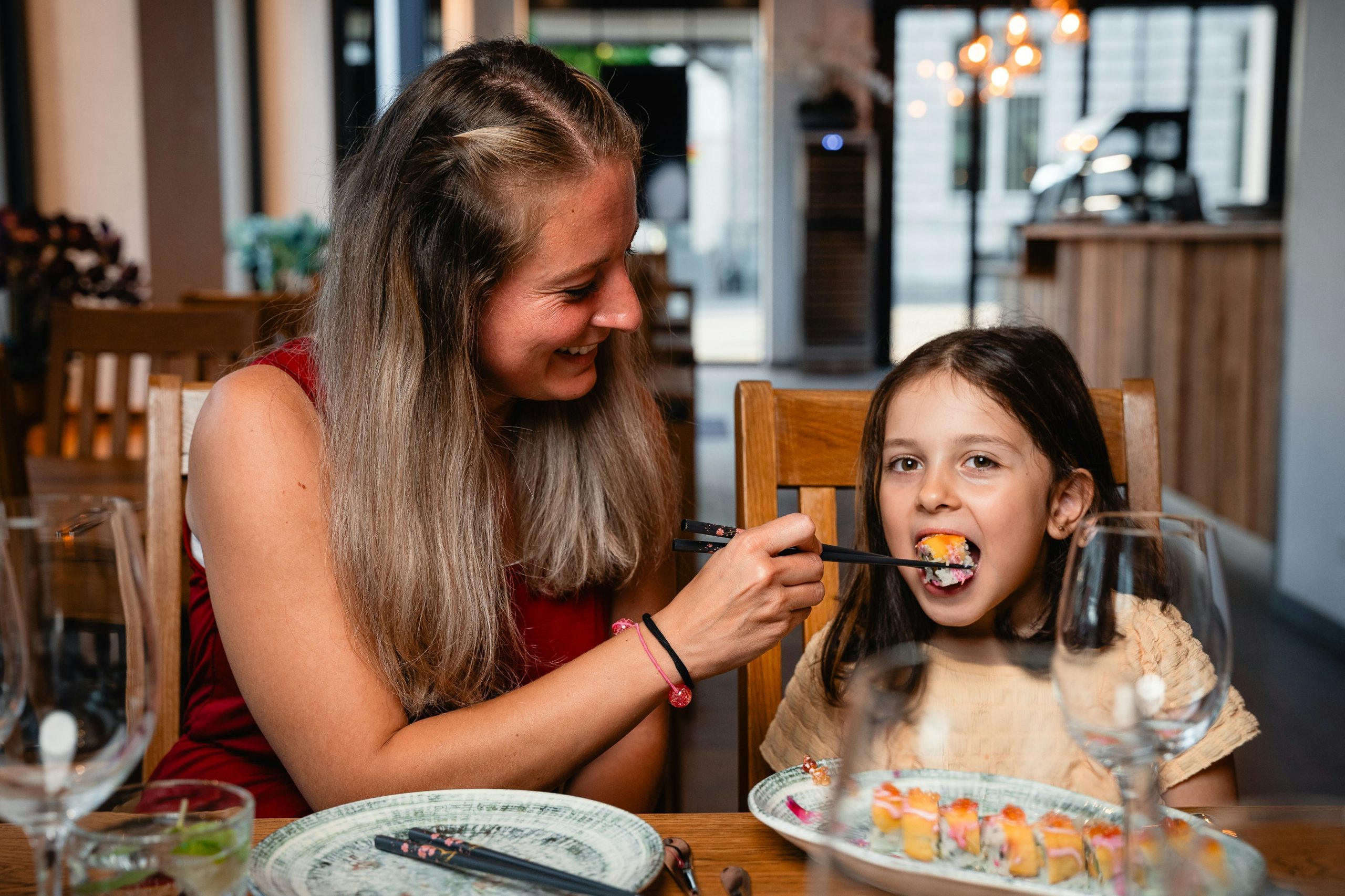 Mother feeds her daughter sushi at a restaurant.
