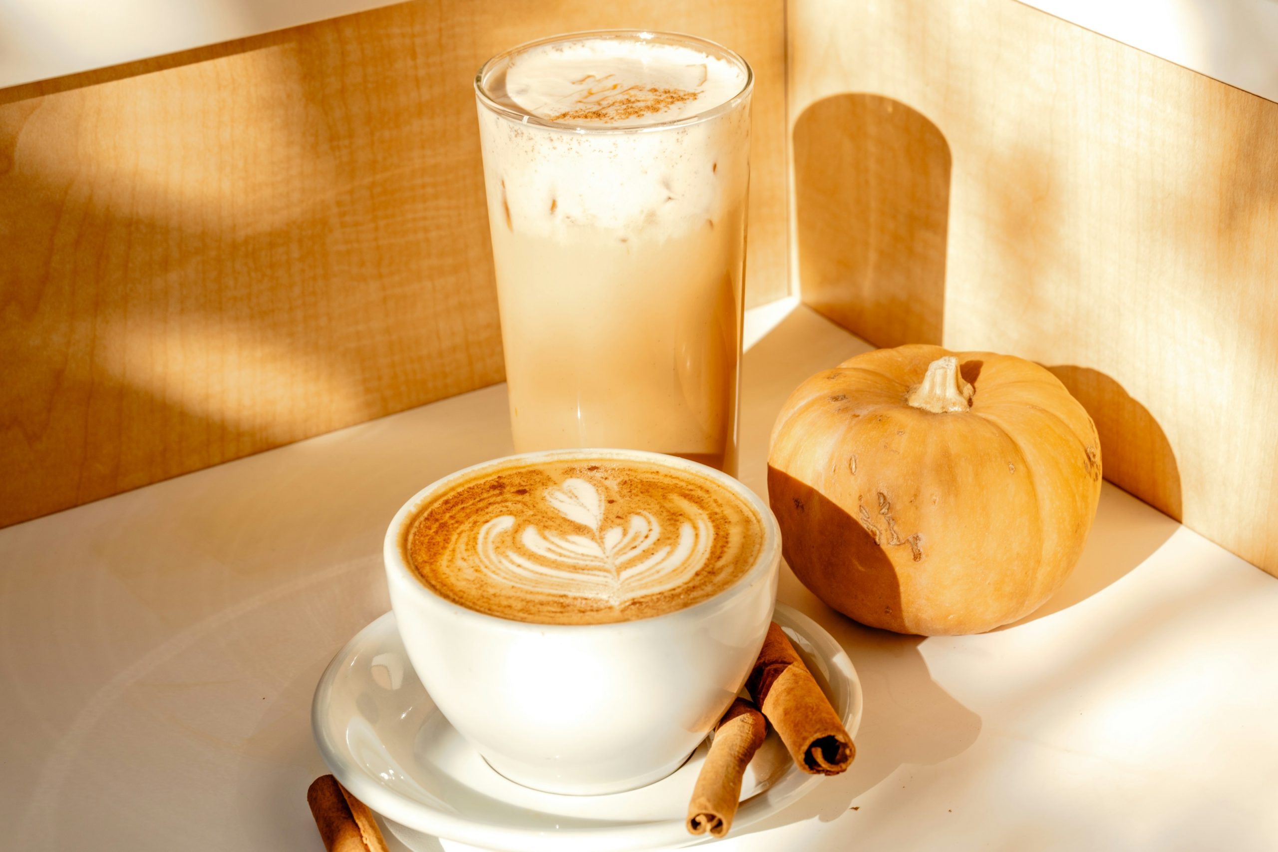 A cup of cappuccino on a saucer next to cinnamon sticks